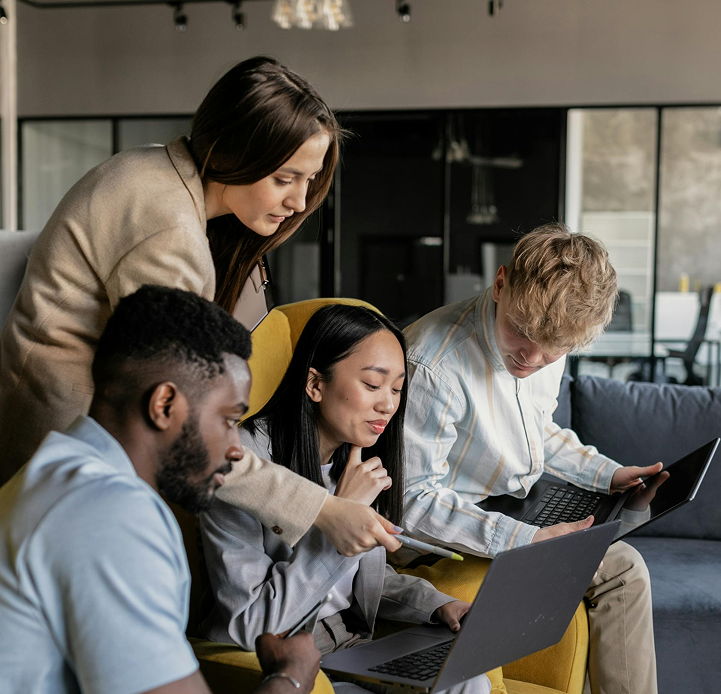 Group of four professionals collaborating on laptops in a modern office setting, sharing ideas and insights.