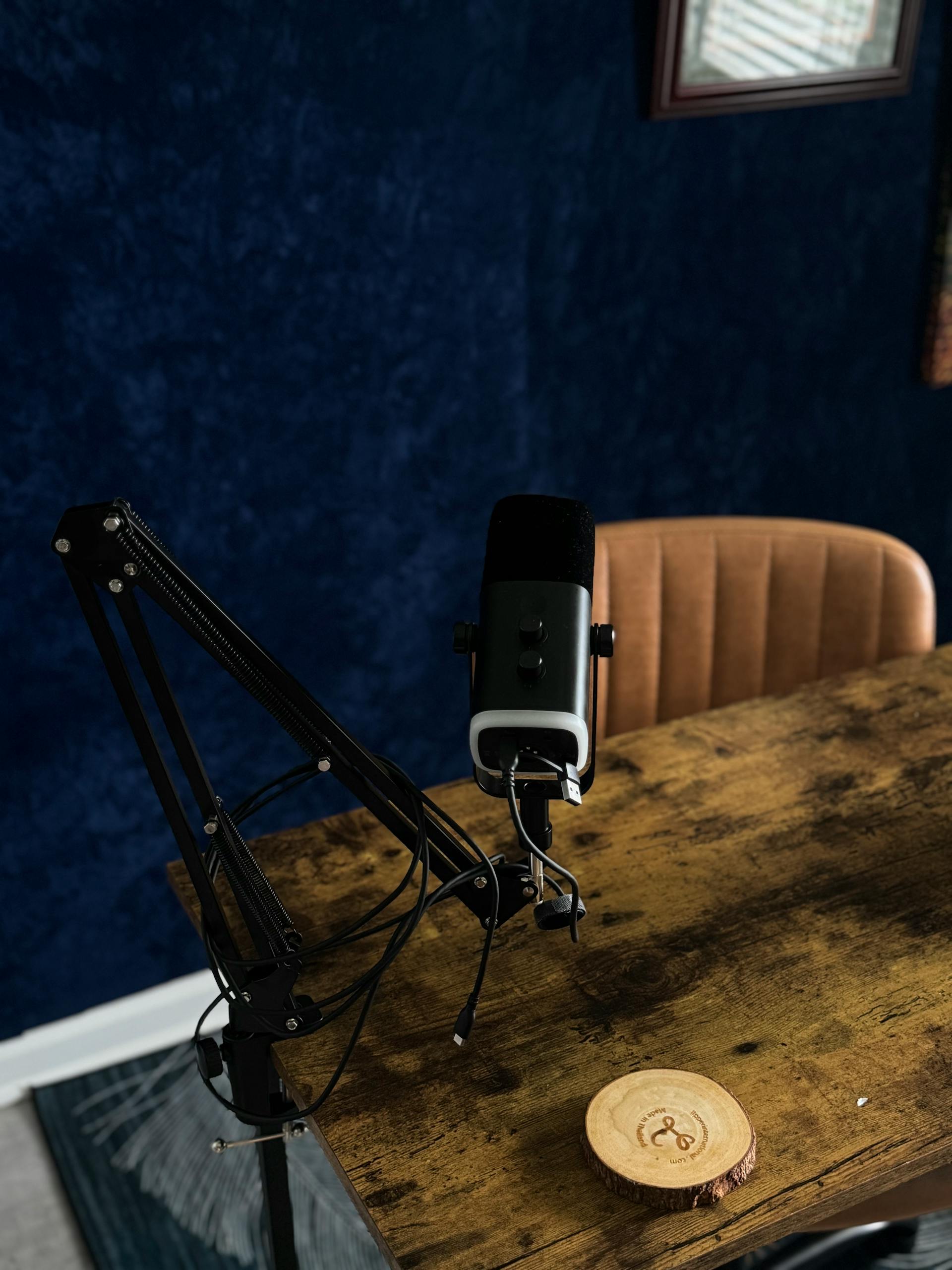 Desktop setup featuring a microphone on an adjustable arm, wooden table, and dark blue wall backdrop.