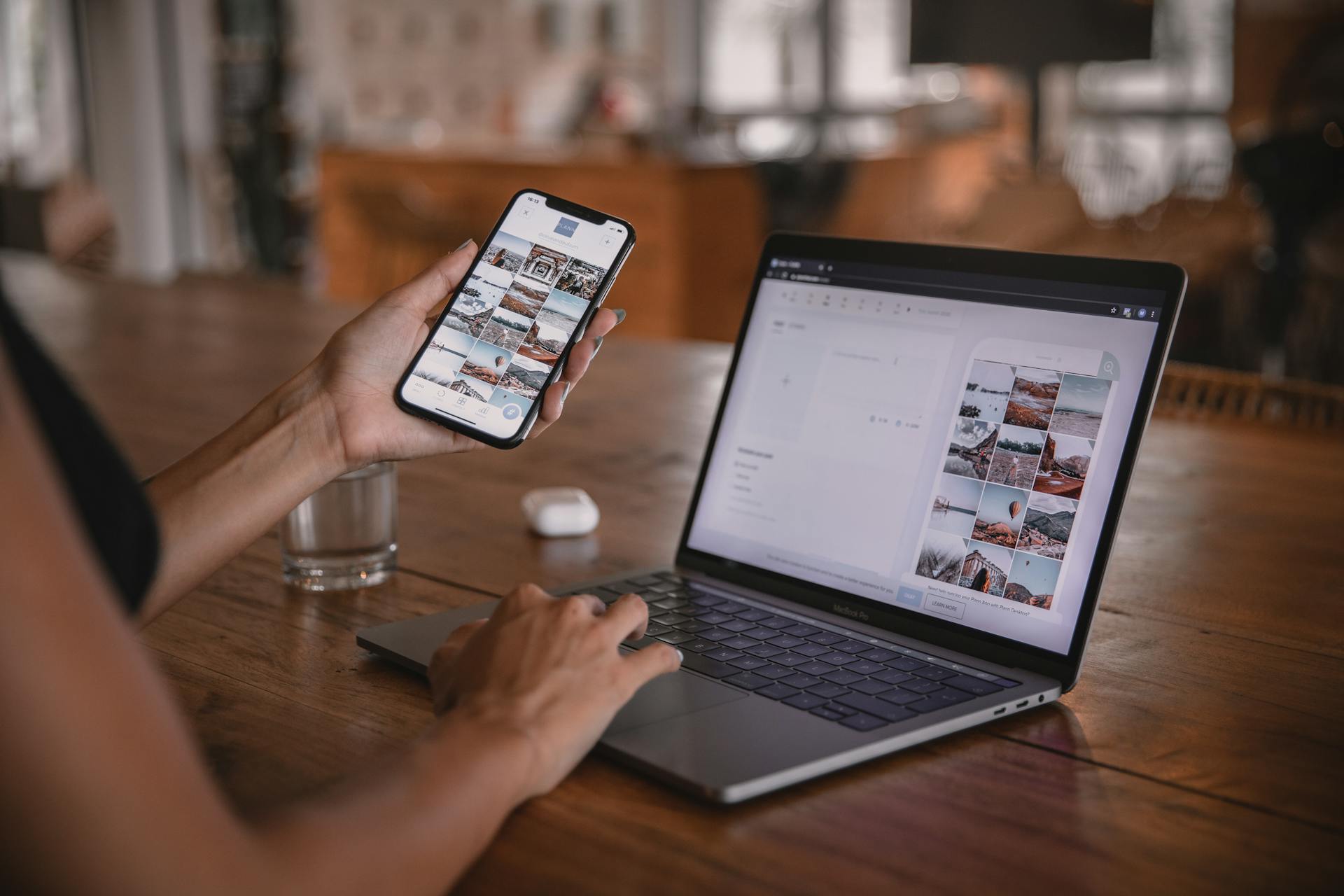 Person using a smartphone and laptop to manage social media content in a modern workspace.
